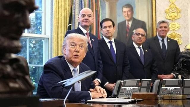 ডোনাল্ড ট্রাম্প বসে আছেন। পেছনে ইনফান্তিনোসহ আরো কয়েকজন দাঁড়ানো।  
